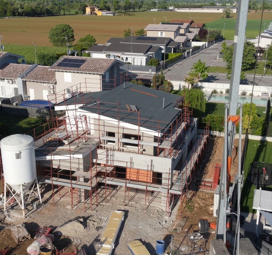 Vista aerea della villa in costruzione: struttura in cemento, ponteggi, una gru e un silo per il cemento sul lotto.