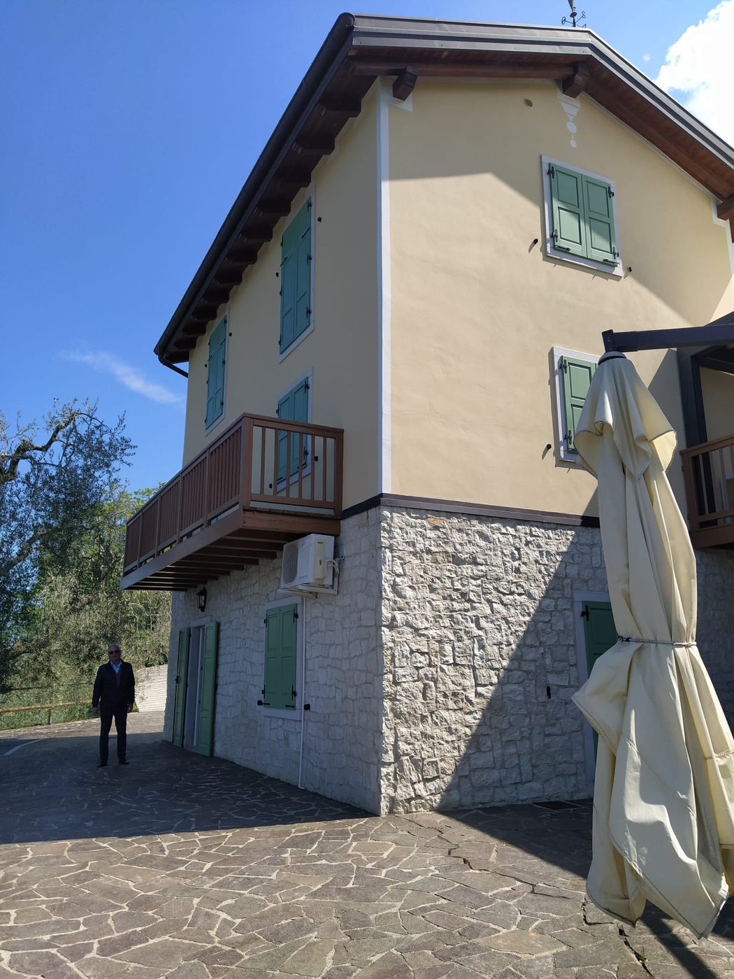 La casa padronale vista da fuori, due piani, con persiane, un balcone e un cortile pavimentato.